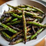 Close-up of vibrant, blistered chinese green beans with garlic sauce piled in a white bowl.