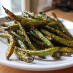 A close-up of blistered, glossy chinese green beans with garlic sauce piled on a white plate.