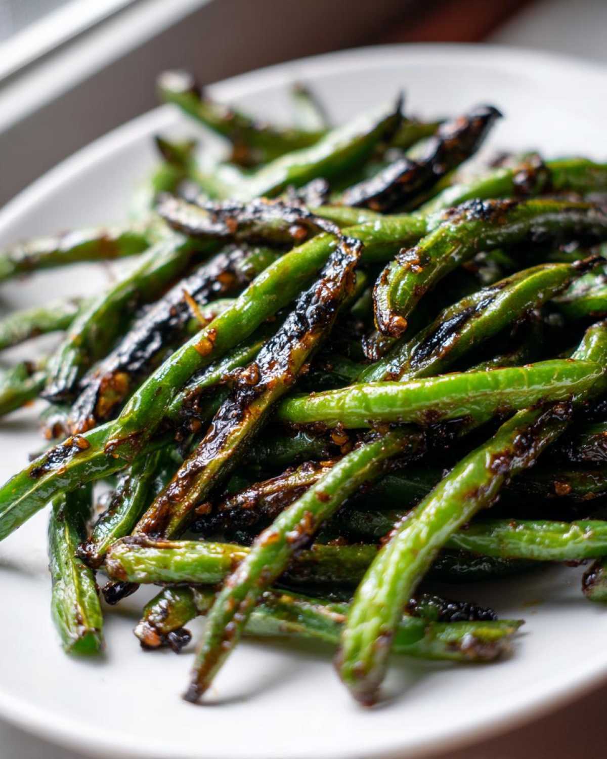 Close-up of blistered, vibrant green chinese green beans with garlic sauce on a white plate.