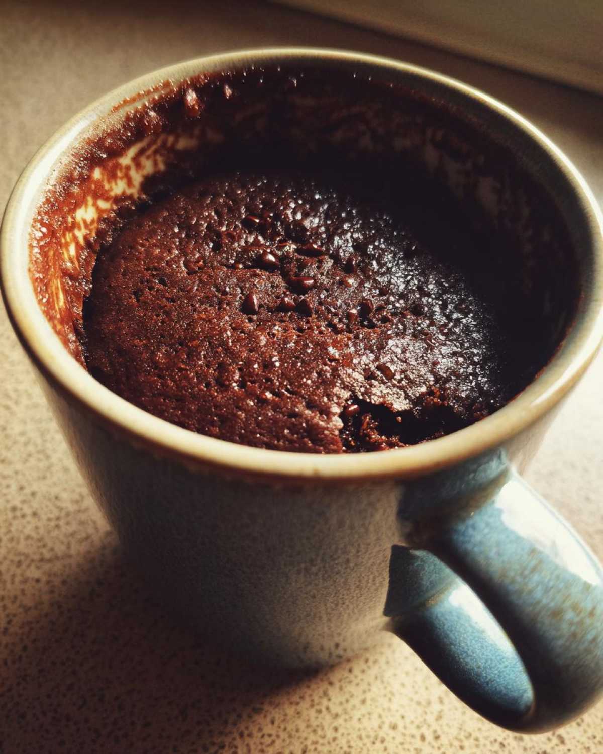 Close-up of a rich, dark chocolate mug cake just finished cooking inside a speckled blue ceramic mug.