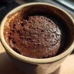 Close-up overhead shot of a rich, dark chocolate mug cake freshly baked inside a rustic ceramic mug.