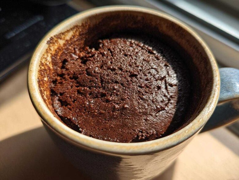 Close-up overhead shot of a rich, dark chocolate mug cake freshly baked inside a rustic ceramic mug.