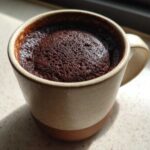 Close-up of a rich, dark chocolate mug cake freshly baked inside a speckled ceramic mug.