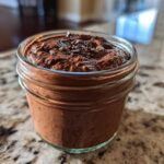 Close-up of creamy chocolate overnight oats topped with chocolate shavings in a small glass jar.