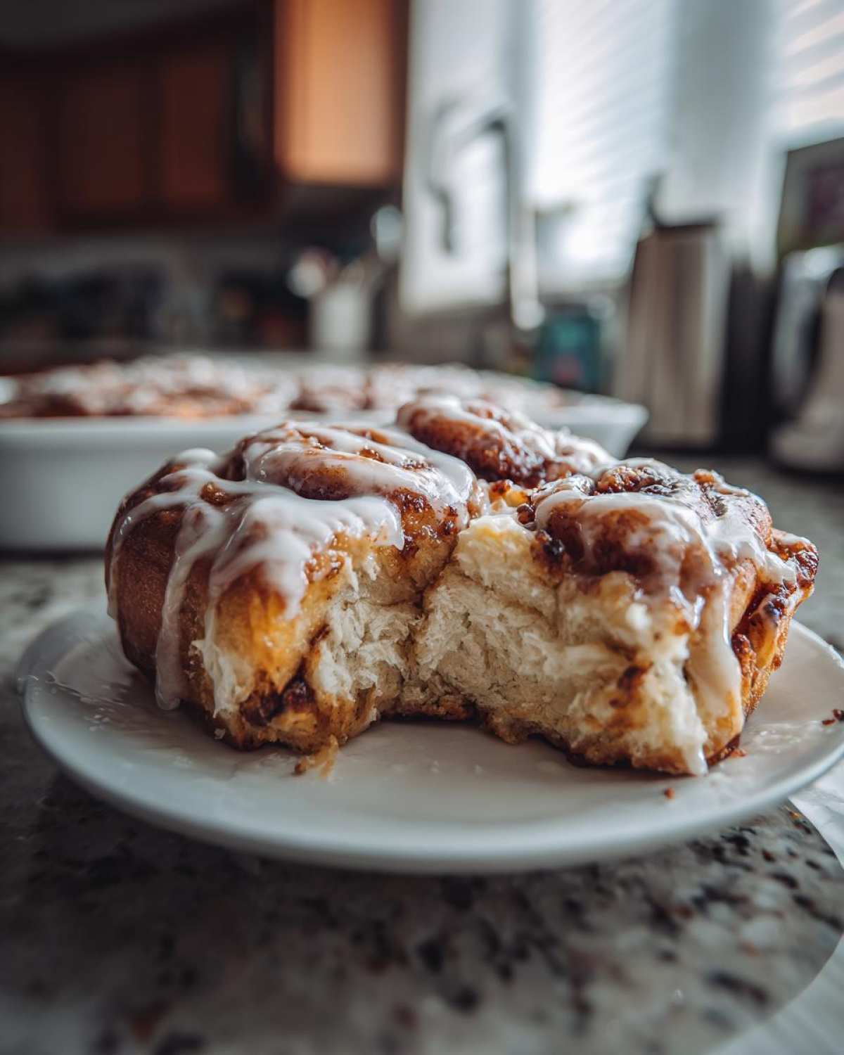 A single, gooey serving of cinnamon roll casserole with white icing, taken from a baking dish.