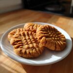 Three golden brown peanut butter cookies with classic criss-cross fork marks served on a white plate.