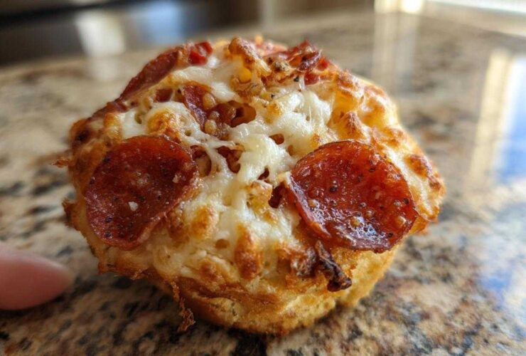 Close-up macro shot of a single, freshly baked pizza muffin topped with melted cheese and pepperoni slices.