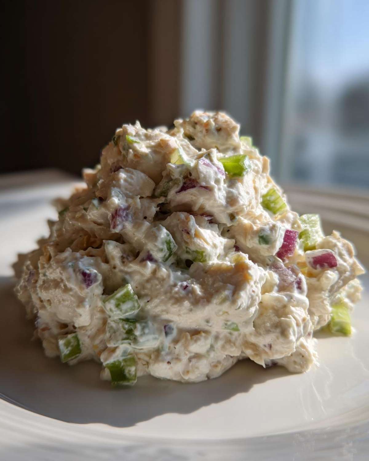 A mound of creamy cottage cheese chicken salad mixed with visible chunks of green celery and red onion on a white plate.