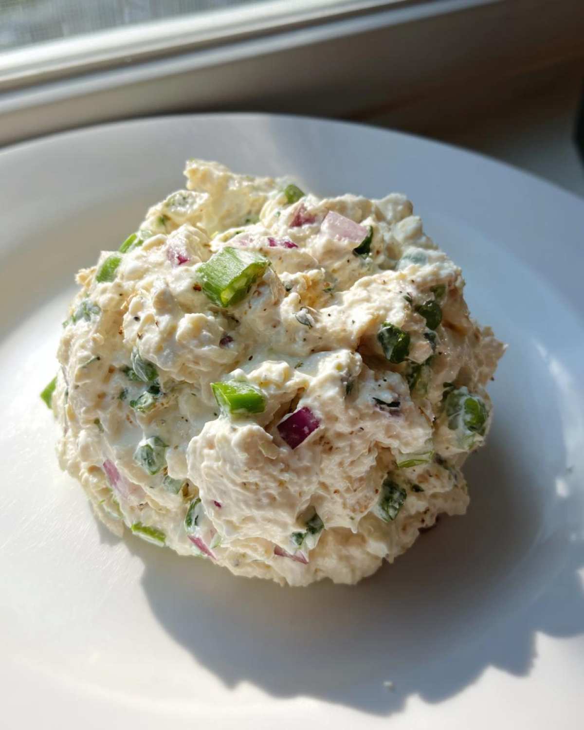 A scoop of creamy cottage cheese chicken salad mixed with visible chunks of red onion and green scallions on a white plate.
