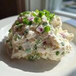 A scoop of creamy cottage cheese chicken salad topped with fresh green onions and red onion pieces.