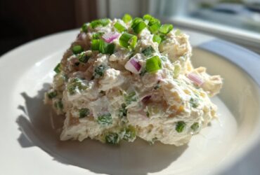 A scoop of creamy cottage cheese chicken salad topped with fresh green onions and red onion pieces.