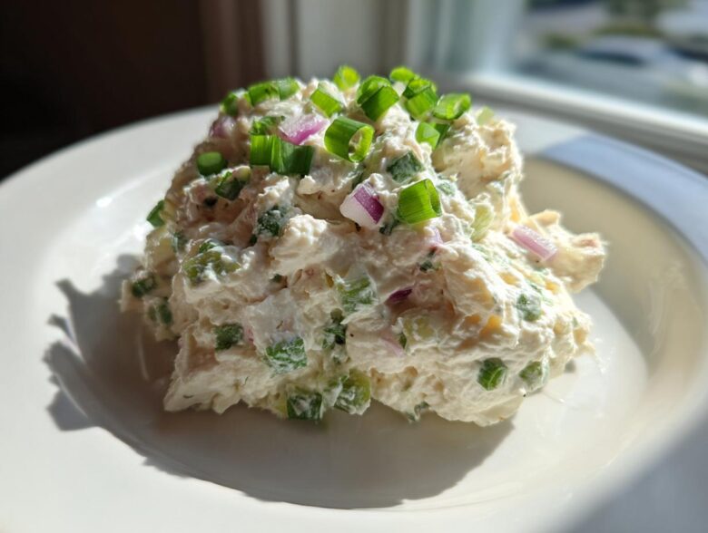 A scoop of creamy cottage cheese chicken salad topped with fresh green onions and red onion pieces.