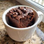 A close-up of a rich, dark chocolate Cottage Cheese Microwave Brownie topped with chocolate chips, served in a white mug.