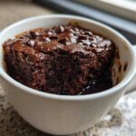 Close-up of a rich, dark chocolate Cottage Cheese Microwave Brownie baked in a white mug, topped with melted chips.