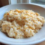 A close-up of a white bowl filled with creamy, warm cheesy rice mixed with melted orange cheddar.