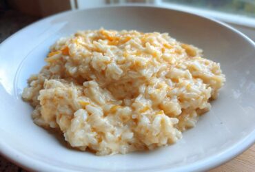 A close-up of a white bowl filled with creamy, warm cheesy rice mixed with melted orange cheddar.