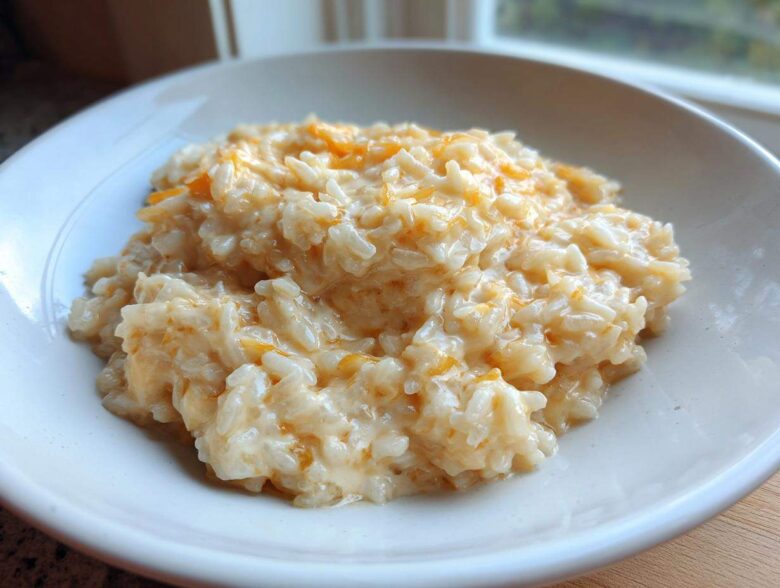 A close-up of a white bowl filled with creamy, warm cheesy rice mixed with melted orange cheddar.