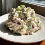 A mound of creamy cottage cheese chicken salad mixed with diced celery and red onion served on a white plate.