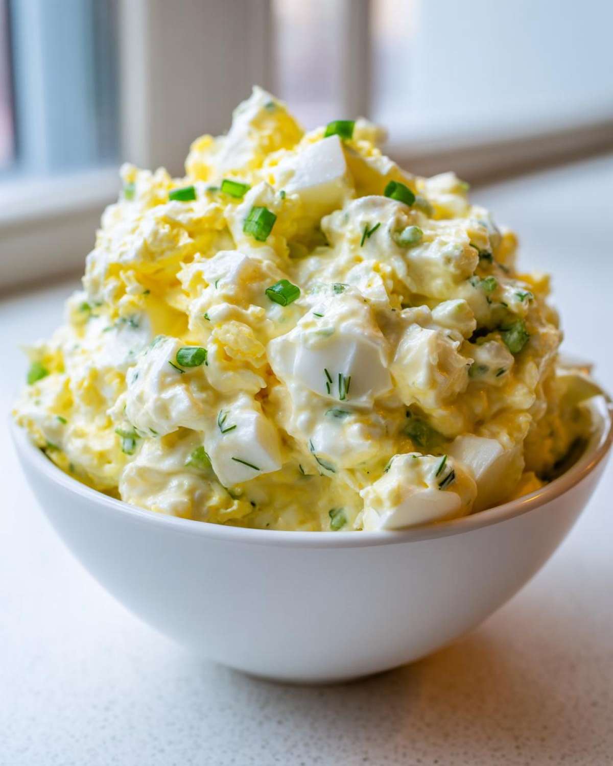 A close-up of a generous serving of creamy egg salad recipe, topped with chopped green onions.