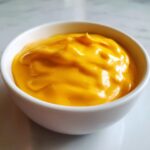 Close-up of thick, vibrant orange nacho cheese sauce served in a small white dipping bowl.