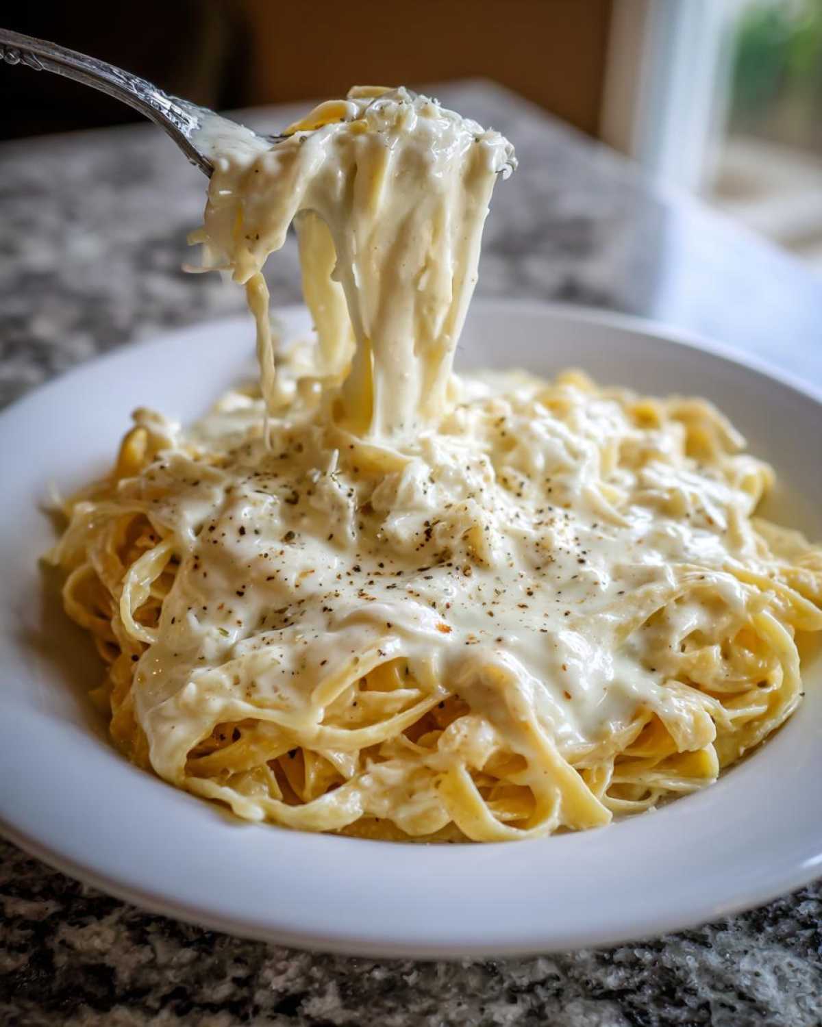 A fork lifts creamy fettuccine coated in rich Olive Garden Alfredo Sauce, topped with black pepper.
