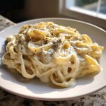 Close-up of pasta coated in rich homemade alfredo sauce, topped with cracked black pepper.