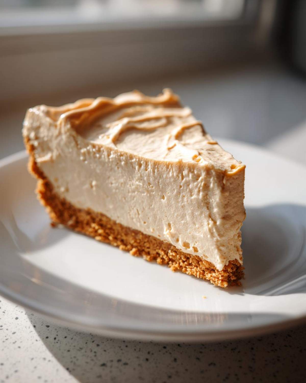 A close-up of a creamy slice of peanut butter pie with a graham cracker crust, served on a white plate.