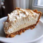 A close-up slice of creamy peanut butter pie featuring a thick graham cracker crust and a fluffy topping.