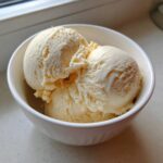 Three generous scoops of creamy, vanilla-colored protein ice cream served in a white bowl.