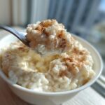 A spoonful of creamy rice pudding topped with cinnamon being lifted from a white bowl.