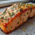 Close-up of a perfectly cooked, crispy air fryer salmon fillet topped with melted butter and fresh parsley.