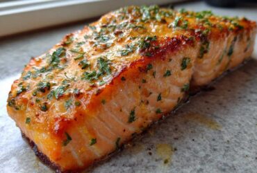 Close-up of a perfectly cooked, crispy air fryer salmon fillet topped with melted butter and fresh parsley.