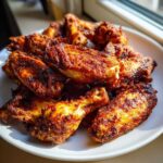 A close-up of a pile of perfectly seasoned and crispy baked chicken wings on a white plate.