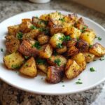 A close-up of perfectly crispy, golden brown breakfast potatoes garnished with fresh chopped parsley on a white plate.
