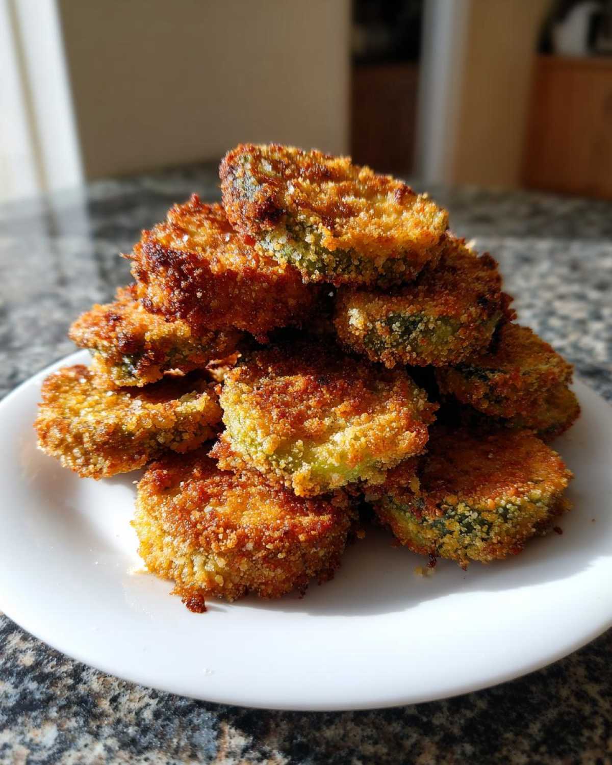 A tall stack of golden brown, crispy Fried Pickles piled high on a white plate, ready to eat.