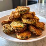 A tall stack of golden brown, crispy fried pickles piled high on a white plate.