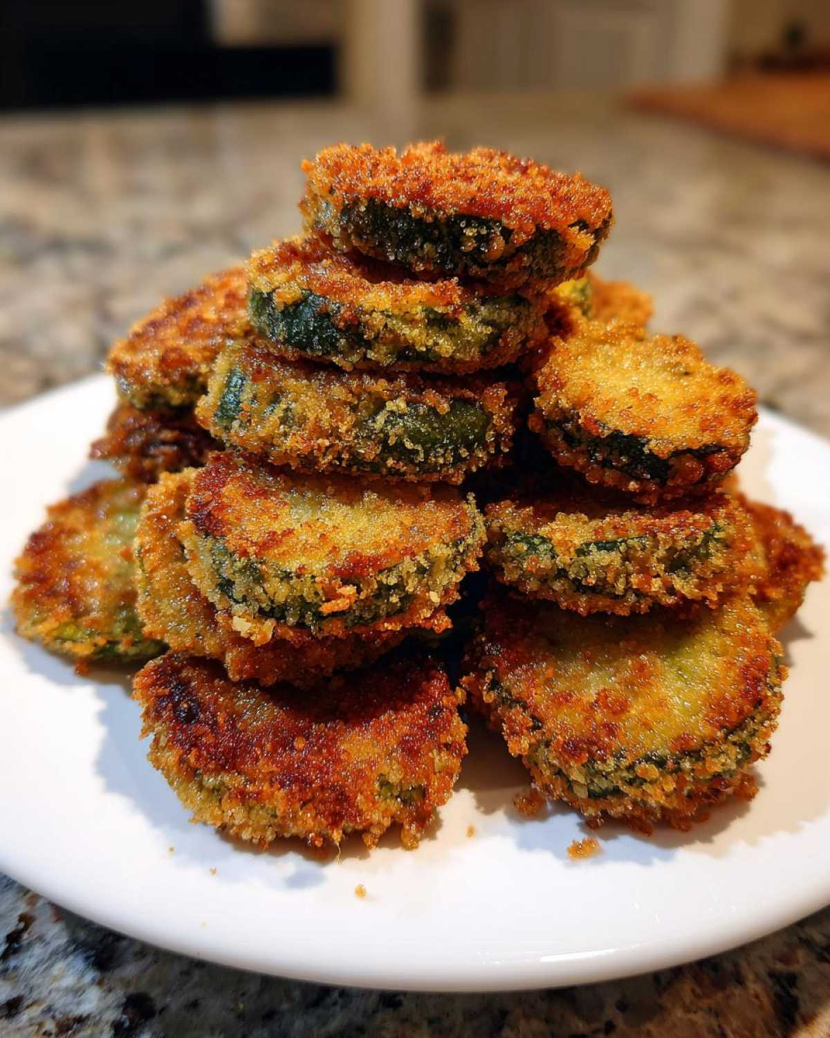 A tall stack of golden brown, crispy Fried Pickles piled high on a white plate.