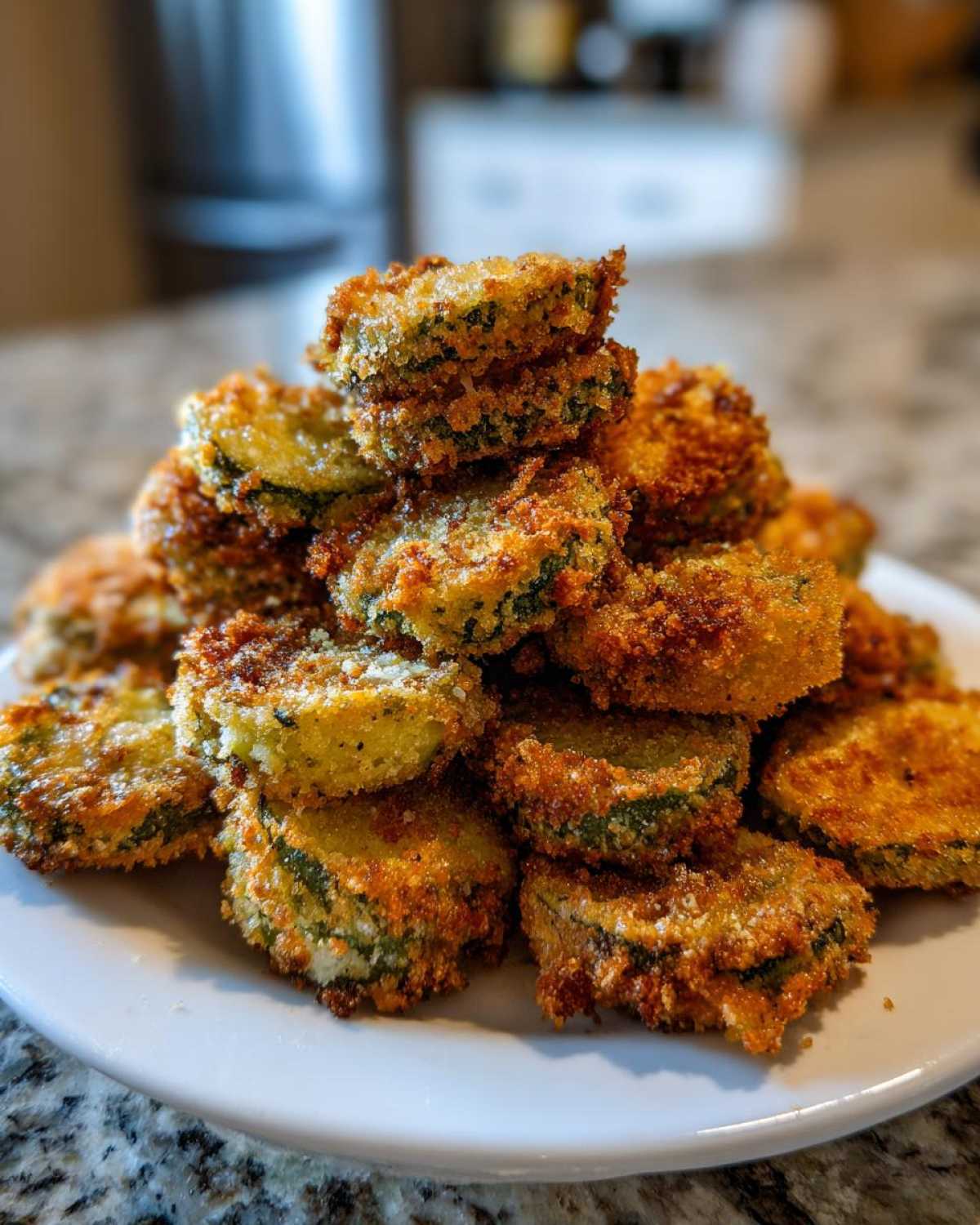 A tall stack of golden brown, crispy Fried Pickles piled high on a white plate, ready to eat.