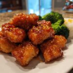 A plate featuring crispy orange chicken recipe pieces coated in a glossy sauce, served with steamed broccoli and white rice.