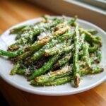A plate piled high with crispy, roasted green beans topped with grated Parmesan cheese.