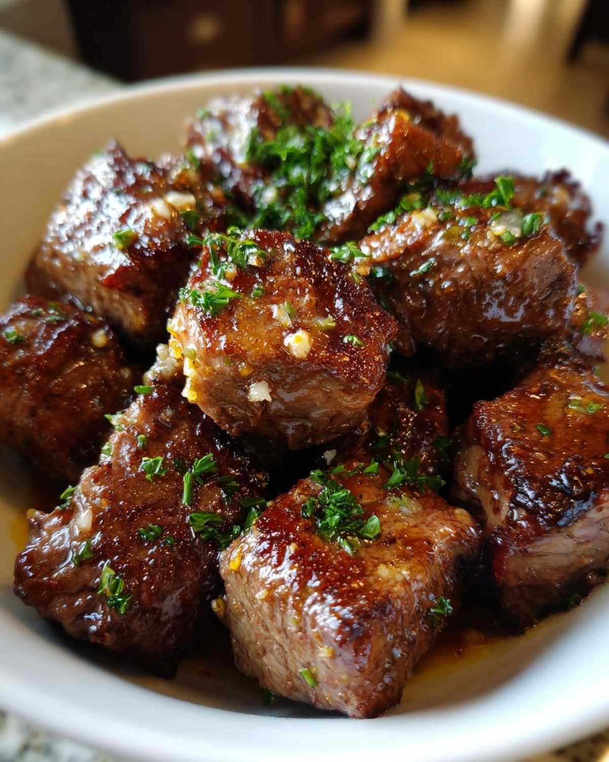 Close-up of tender, cubed crockpot steak pieces coated in a rich, glossy sauce and topped with fresh parsley.