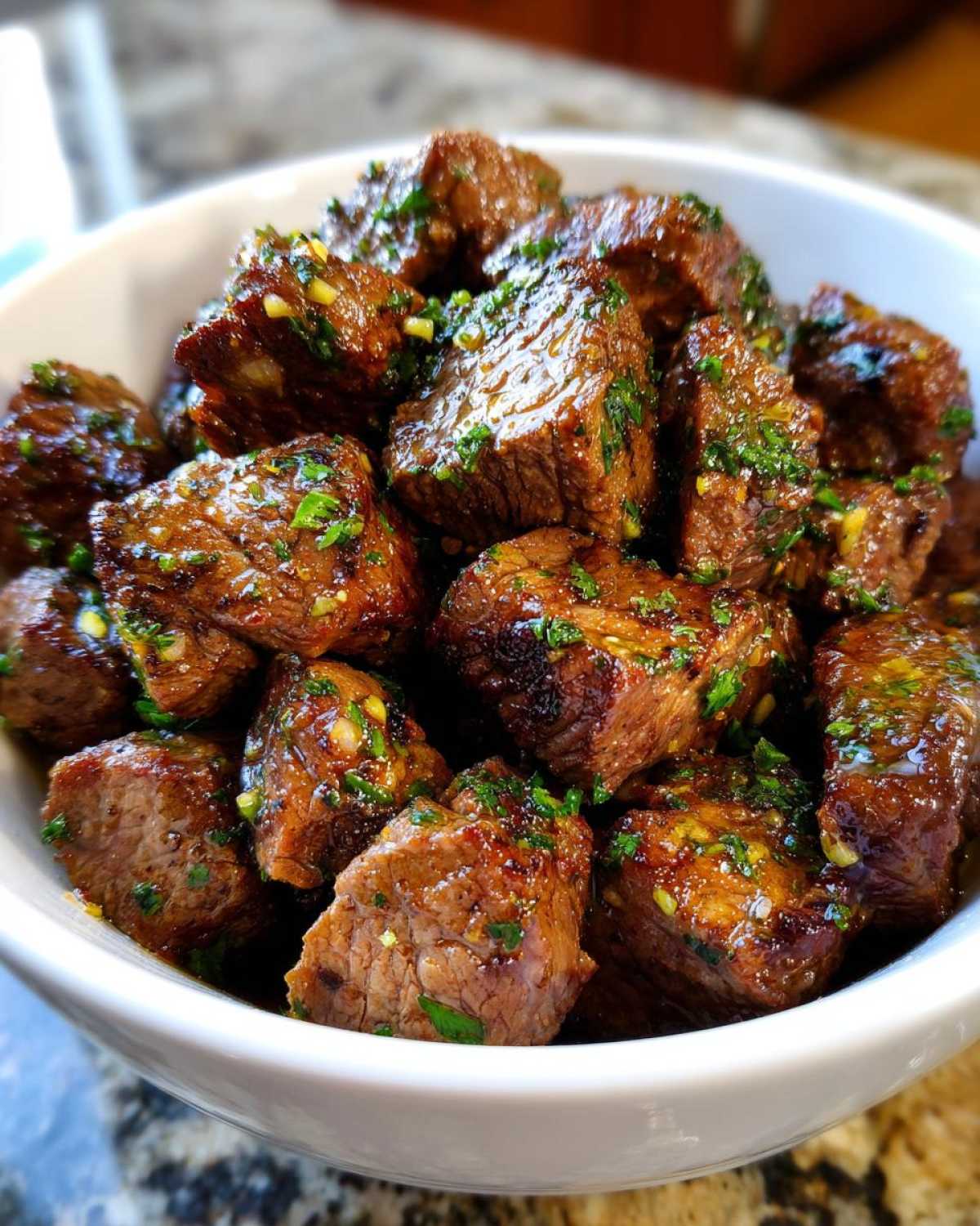 Close-up of tender crockpot steak bites seasoned with garlic and parsley in a white bowl.