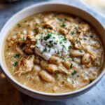 A close-up of a creamy bowl of crockpot white chicken chili topped with sour cream and fresh parsley.