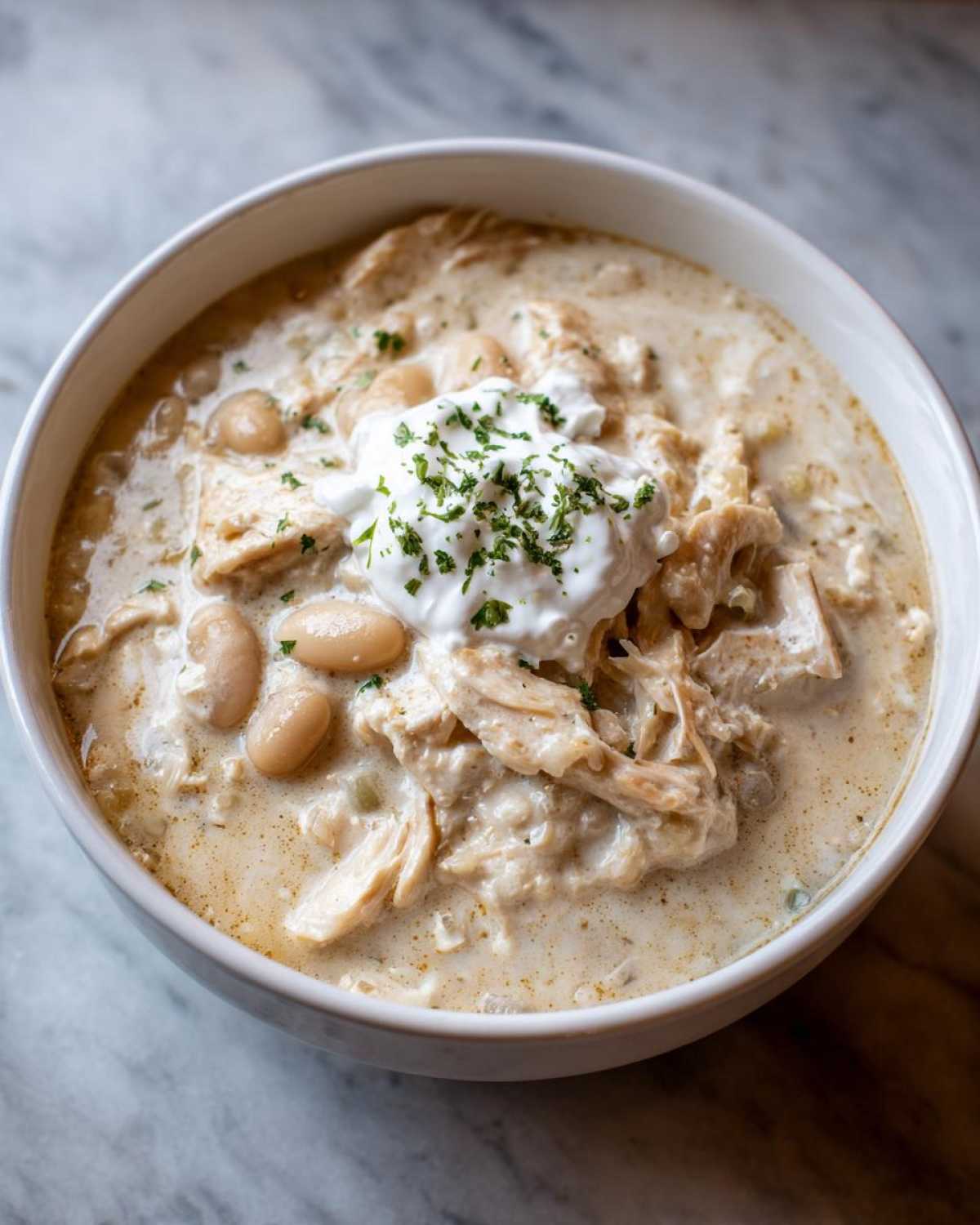 Close-up of a bowl of creamy crockpot white chicken chili topped with sour cream and parsley.