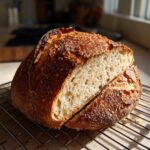 A freshly baked loaf of Italian bread, sliced open to show the airy interior, resting on a cooling rack.