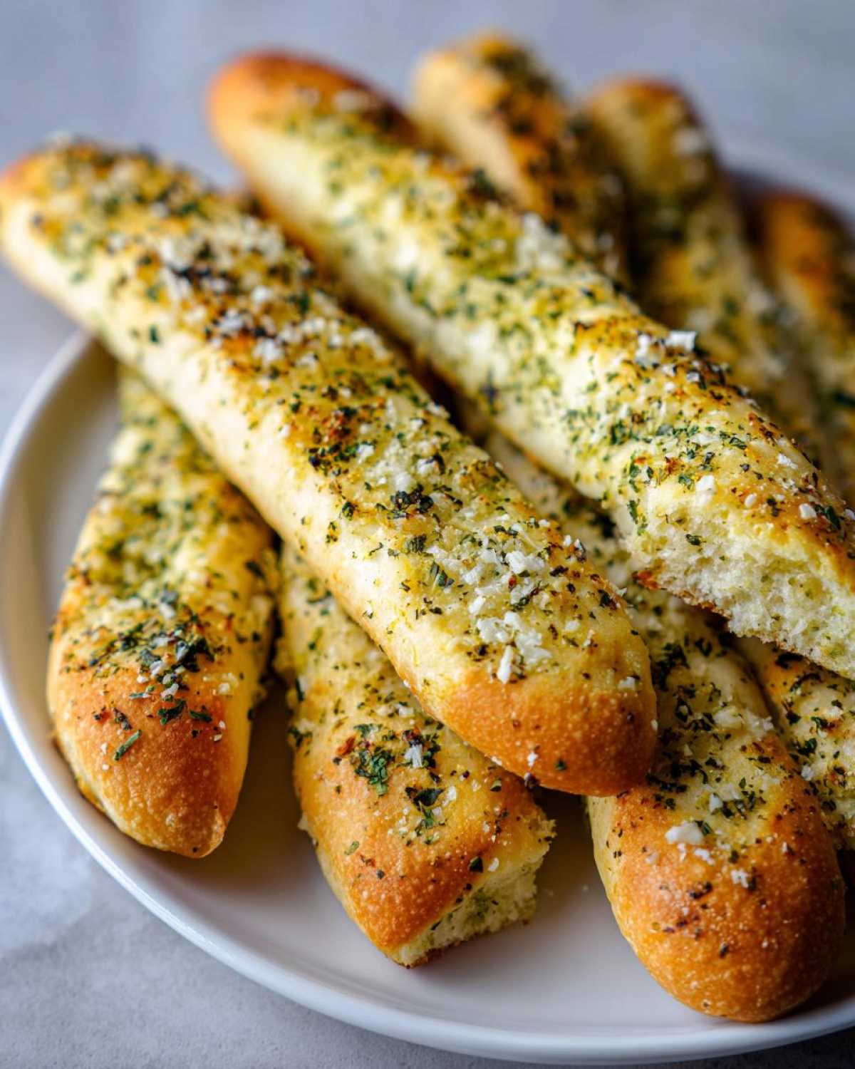Close-up of golden brown, soft breadsticks generously topped with garlic, herbs, and cheese.