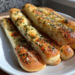 Close-up of several golden brown, soft breadsticks topped with garlic, herbs, and Parmesan cheese.