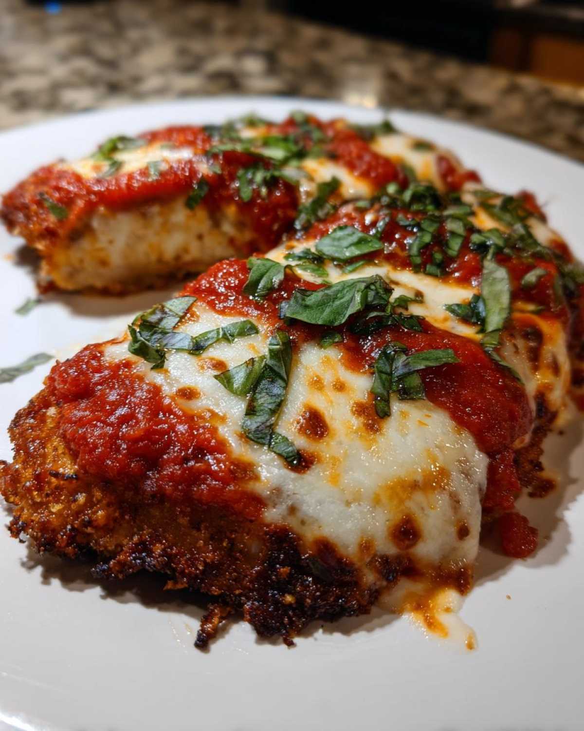 Close-up of two servings of Easy Chicken Parmesan topped with melted mozzarella, marinara sauce, and fresh basil.