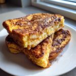 A stack of three thick slices of golden brown easy french toast dusted with cinnamon on a white plate.