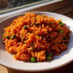 A close-up of vibrant orange spanish rice mixed with bright green peas served on a white plate.